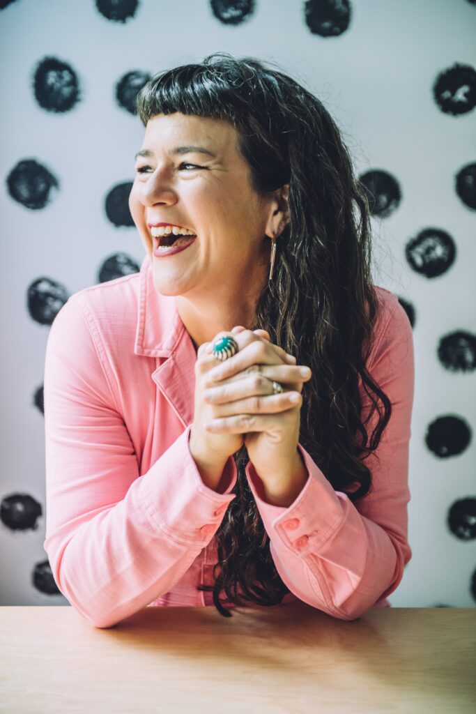 Life coach Beatriz Victoria Albina in a pink jumpsuit, smiling while sitting at a table