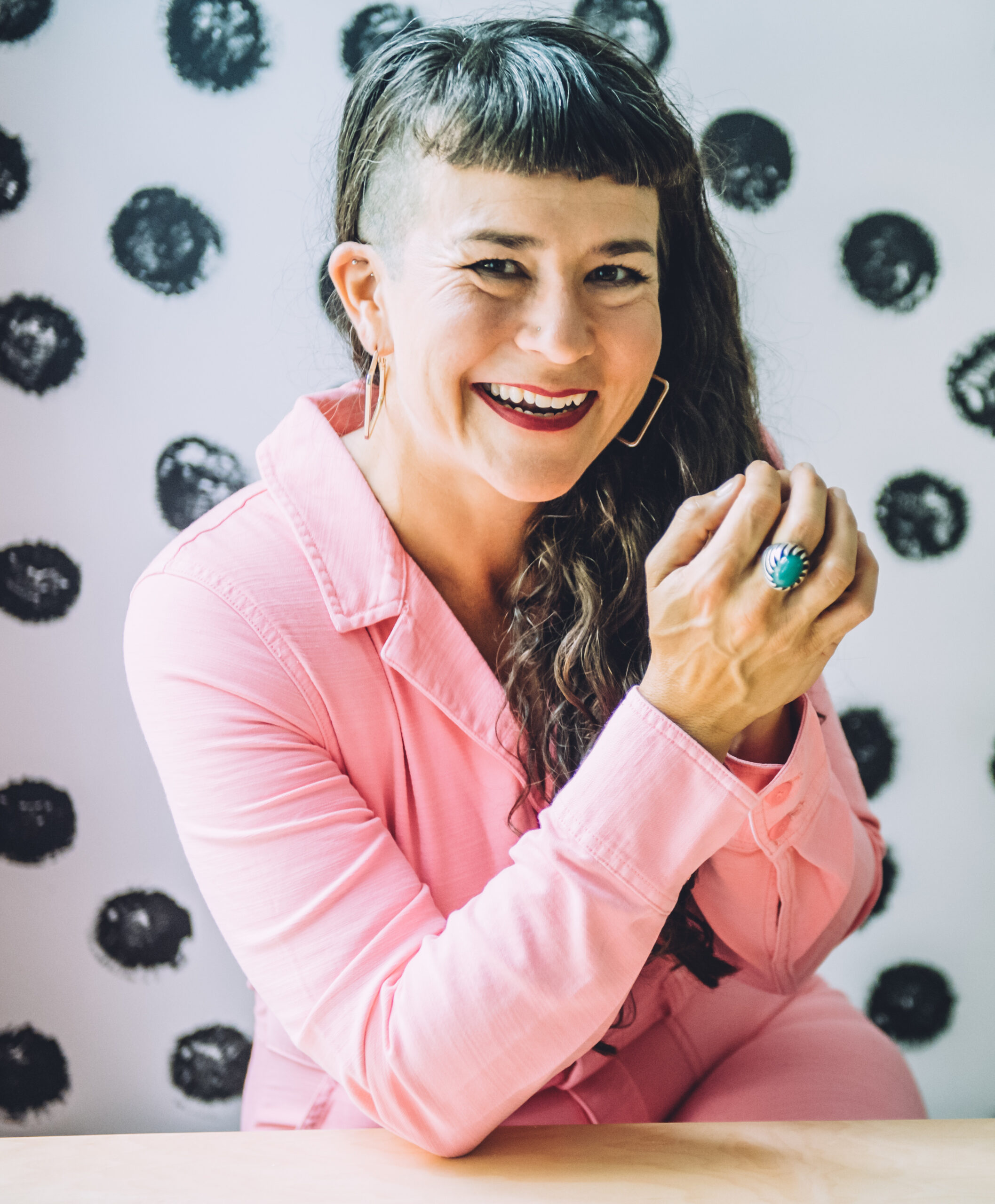 Life coach Beatriz Victoria Albina in a pink jumpsuit smiling and sitting at a table