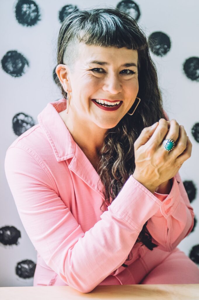 Life coach Beatriz Victoria Albina wearing pink coveralls and sitting in front of a polka dot wall