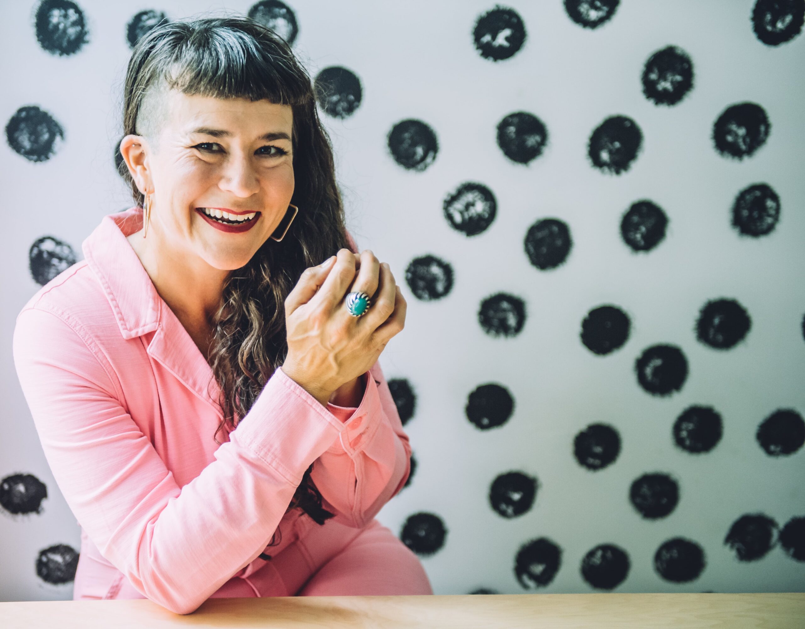 Life coach Beatriz Victoria Albina wearing pink coveralls sitting in front of a polka dot wall