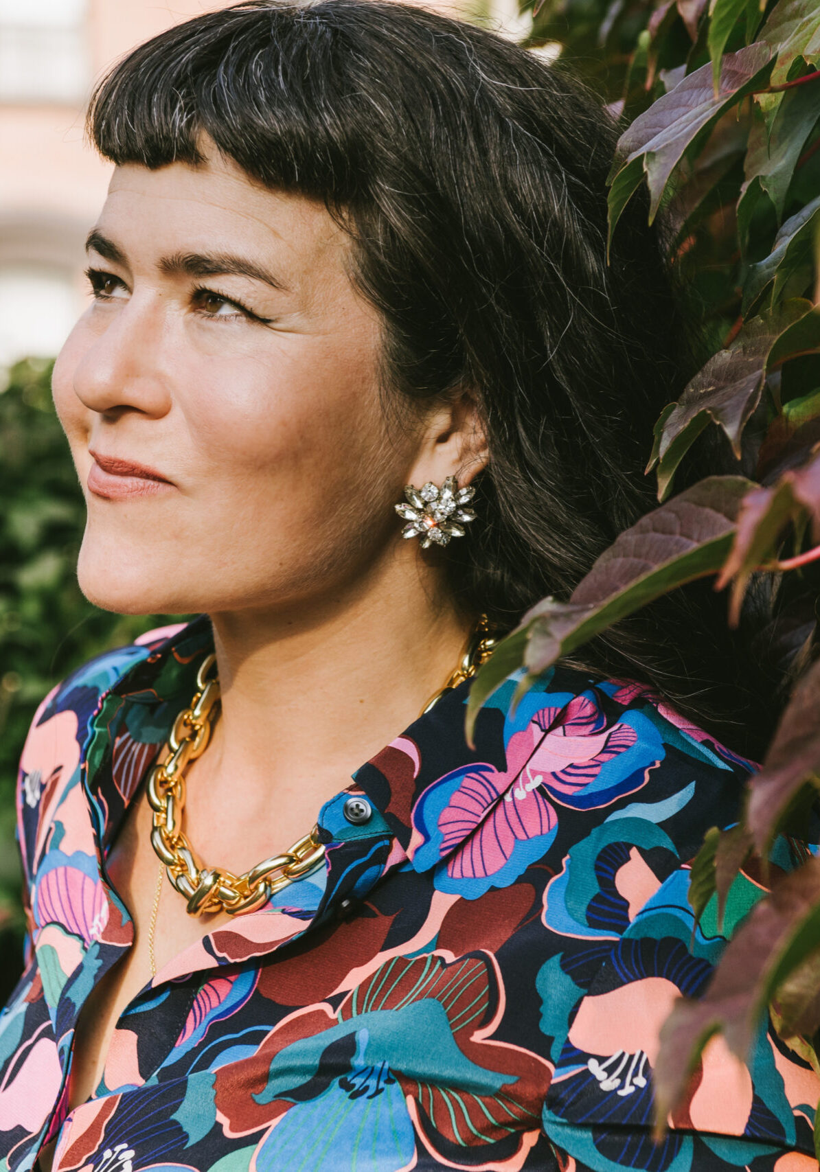 Codependency coach Beatriz Victoria Albina in a floral blouse looking up and standing next to a hedge