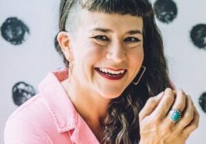 Life coach Beatriz Victoria Albina wearing pink coveralls sitting in front of a polka dotted wall